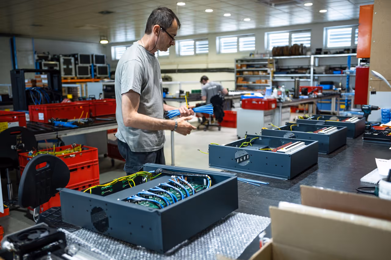 Technik osádza zväzky vodičov do plechových skríň na montážnom stole vo výrobnej hale